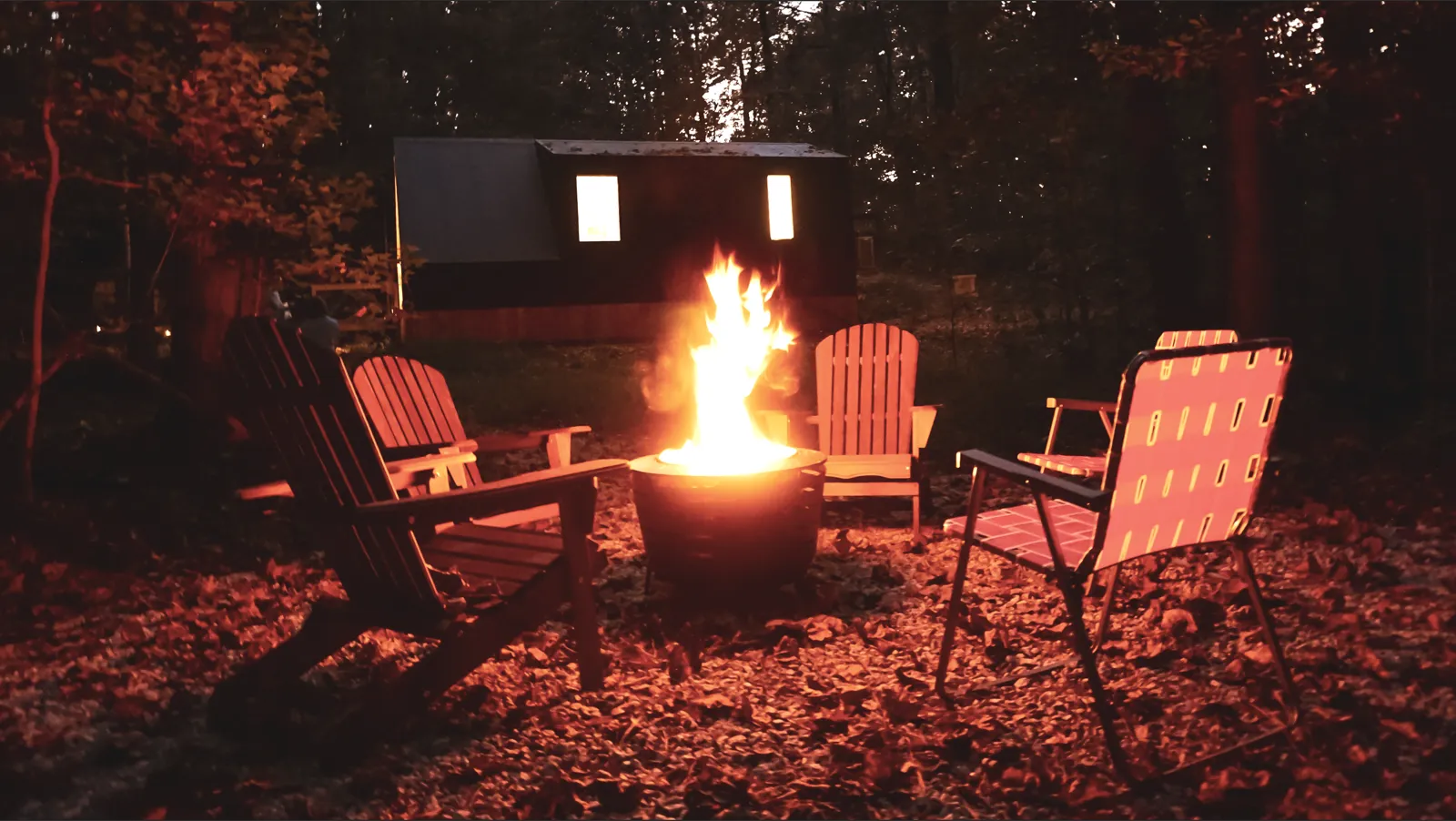 Blazing smokeless fire pit at night with the glowing barrel sauna behind