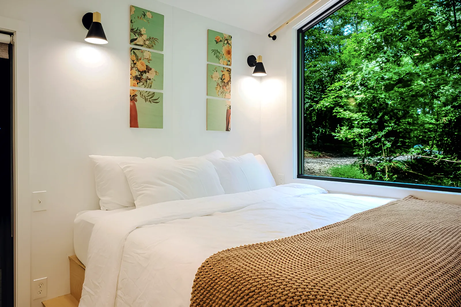 King bed with white linens beside a picture window filled with dense green forest