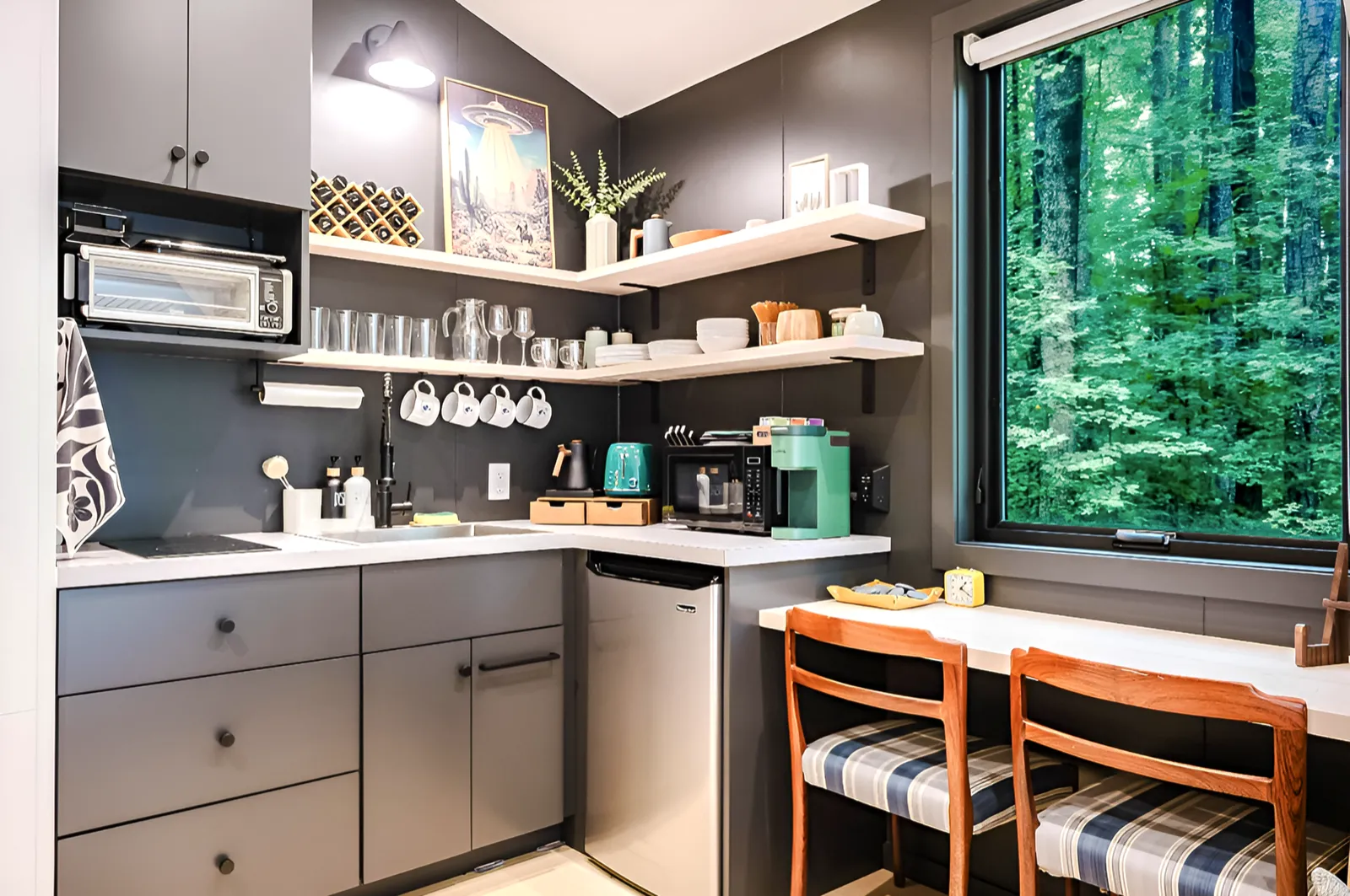 Kitchenette with open shelving, coffee bar, and two-seat counter beside a forest-view window